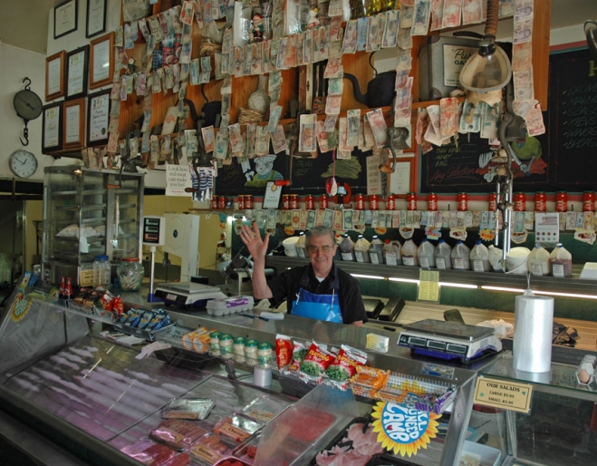 Butcher waving behind counter covred in foreign bank notes inside Annerley Meats in Brisbane.