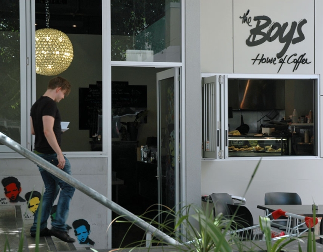 Waiter carrying cup of coffee walking down steps outside boys house of coffee in Kelvin Grove.
