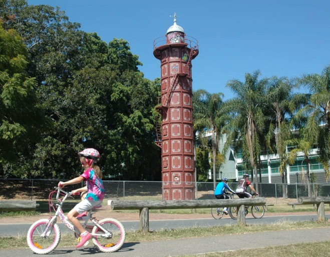 Kids riding a bike in front of Gas Stripping Tower near Davies Park in West End