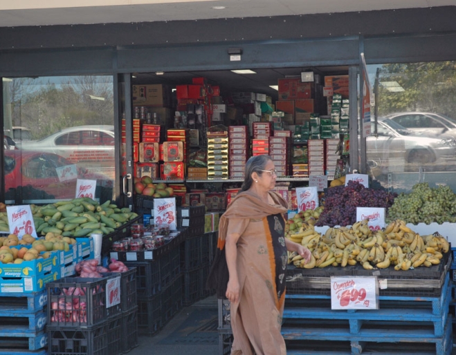 Indian woman in sari walking in front of K &amp; K Fresh Food Market in Darra.