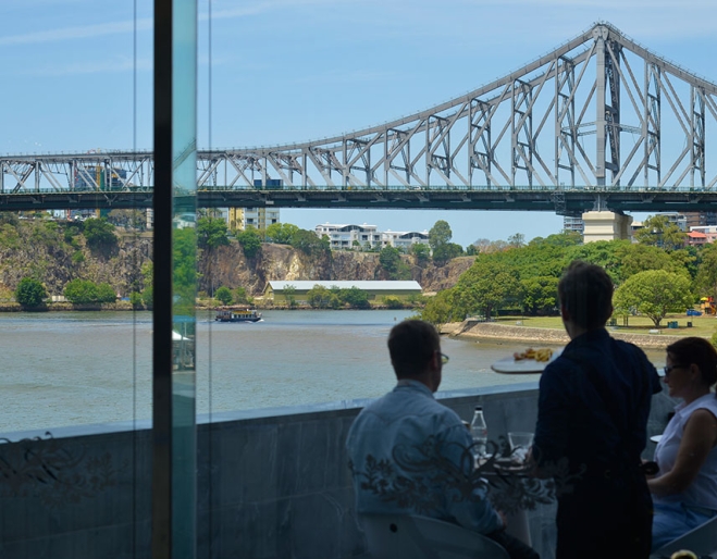 Couple sitting at table on deck overlooking the Story Bridge and Brisbane River