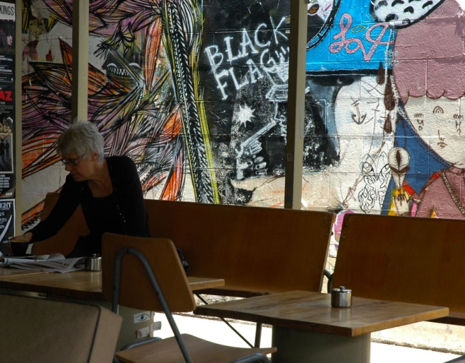 Woman sitting at table drinking coffee next to stencil artwork on wall inside Black Star Coffee Roastery in Brisbane's West End