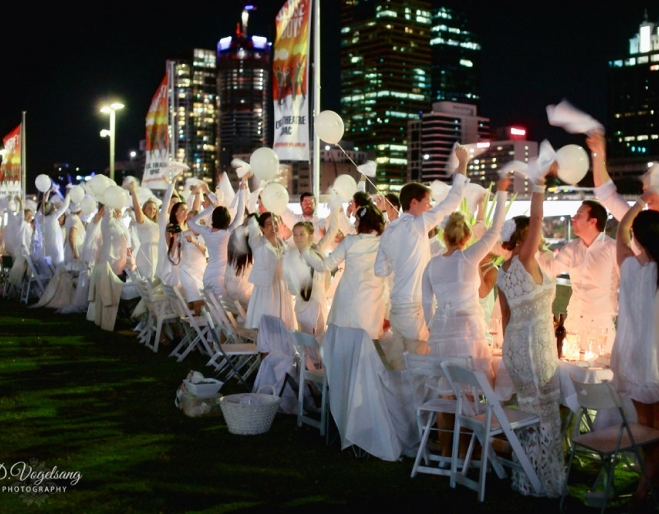 people dressed in white at tables on astro turf along the Brisbane River during the Diner en Blanc event in Brisbane