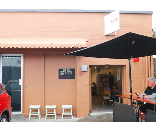 Man sitting under an umbrella at a table outside Mad Mile Coffee