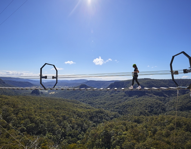 Woman on an 80-metre wobbly bridge at The Arête Via Ferrata Tour at Happitat Adventure Park 