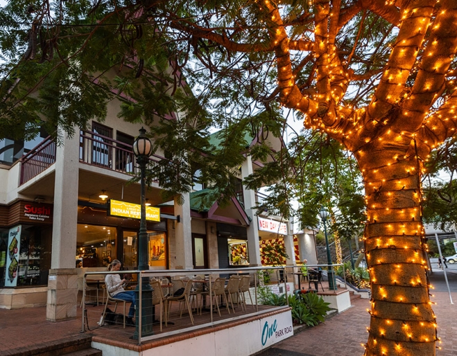 Woman sitting at table next to fairy-lit tree outside A Night in India Milton