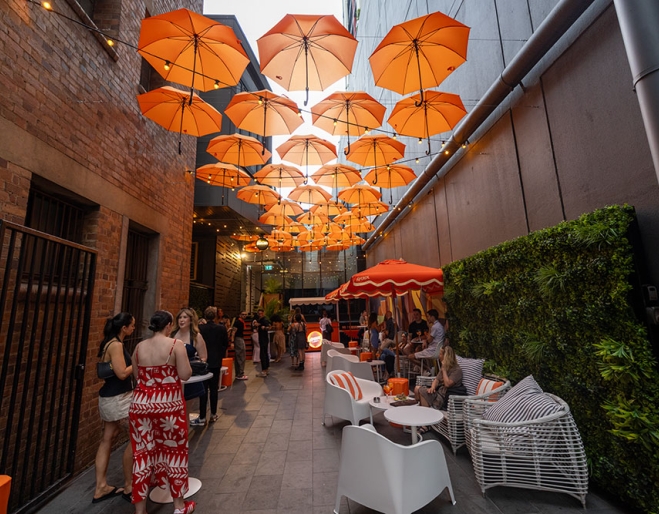 People seated under orange umbrellas in Doughcraft Lane