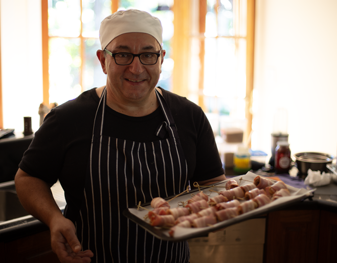 Chef Robert Bousamra standing in kitchen holding tray of food