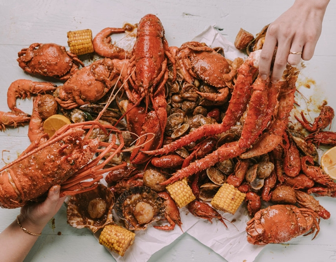 Two hands grabbing pieces of crab at Krabby’s Crab Boil, The Barracks, Petrie Terrace