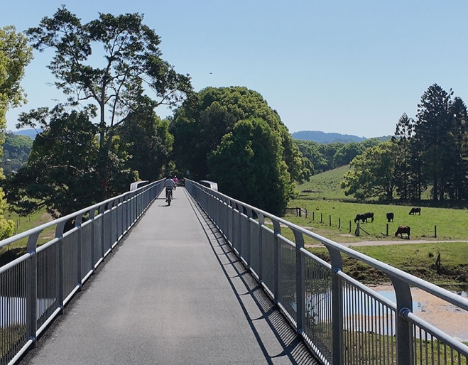 Cyclist on e-bike crossing rail bridge overlooking lush countryside