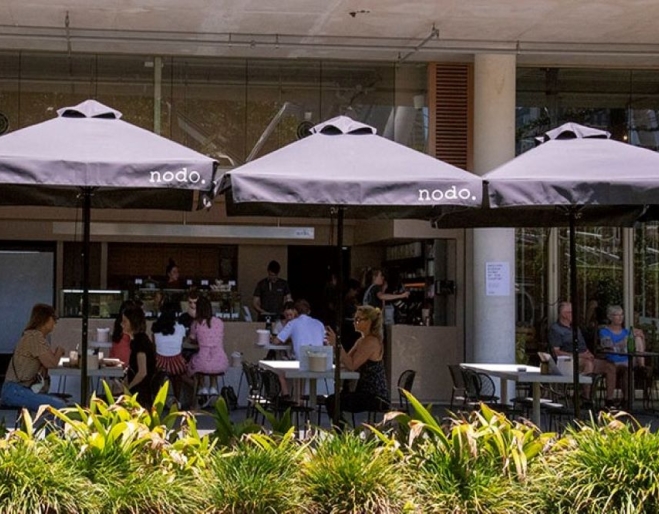 People sitting under umbrellas in courtyard at Nodo South 