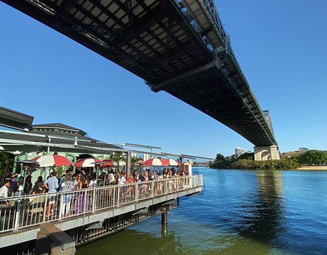 People dining at open air cafe under bridge next to Brisbane River