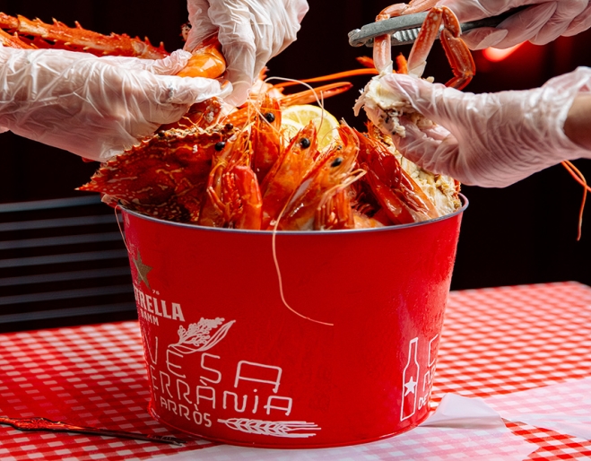 Bucket of crab with two pairs of gloved hands grabbing pieces