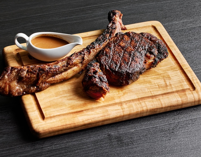 T-bone steak on chopping board with sauce cup