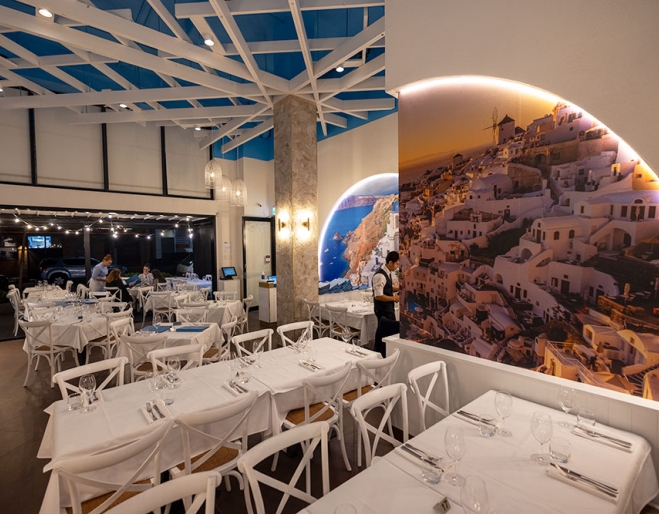 Tables and chairs with white tablecloths and mural on wall inside Santorini Restaurant, Newstead