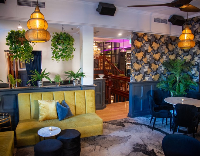 Yellow banquette, wallpaper and chandelier at Trove Bar