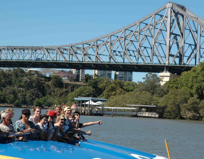 Passengers waving on board Rivercat Ferry in fron of  Brisbane's Story Bridge.