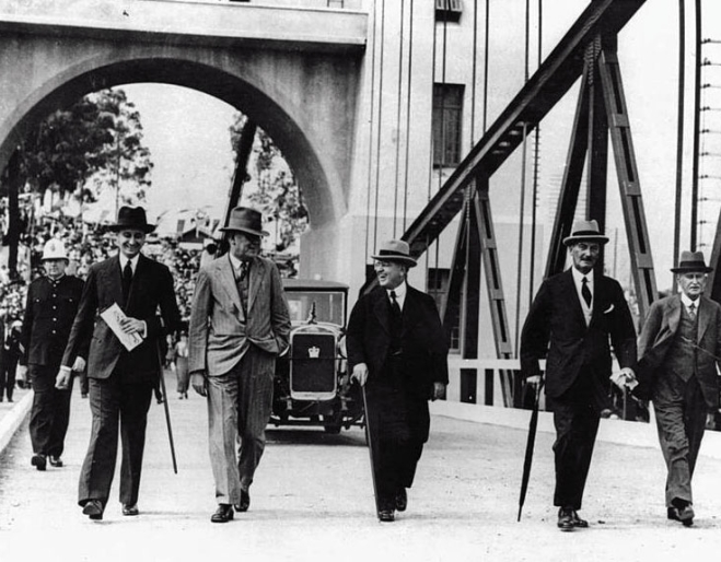 Old black and white photo of five men wearing suits and hats walking along Indooroopilly