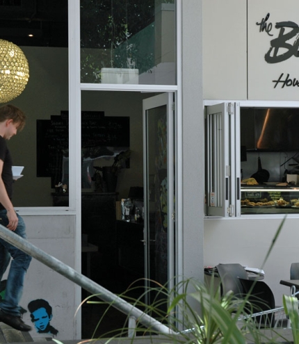 Waiter carrying cup of coffee walking down steps outside boys house of coffee in Kelvin Grove.