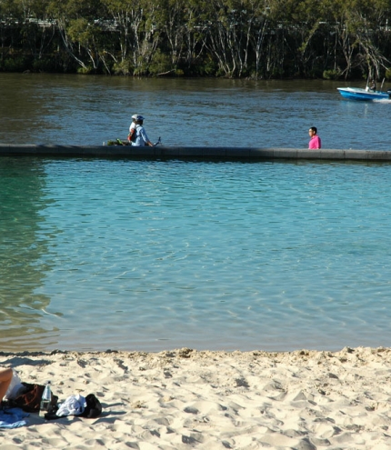 Woman lying on Streets Beach looking at speed boad on Brisbane River and mangroves.