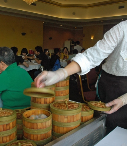 Waitress serving yum cha out of bamboo steaming boxes on a trolley