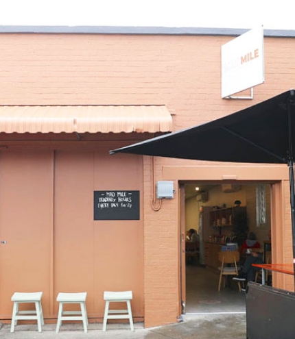 Man sitting under an umbrella at a table outside Mad Mile Coffee