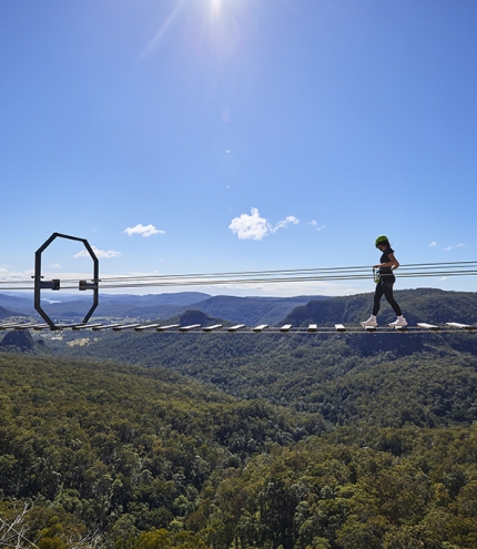 Woman on an 80-metre wobbly bridge at The Arête Via Ferrata Tour at Happitat Adventure Park 