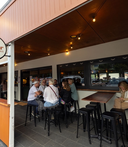 Exterior of Clover Neighbourhood Bar Holland Park with people sitting on bar seats