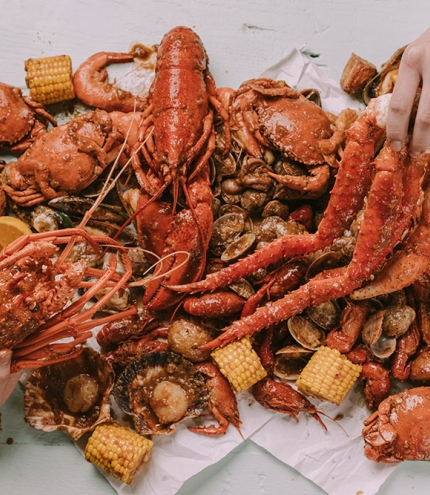 Two hands grabbing pieces of crab at Krabby’s Crab Boil, The Barracks, Petrie Terrace