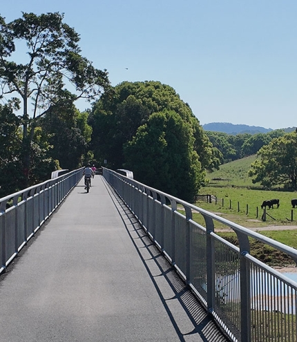 Cyclist on e-bike crossing rail bridge overlooking lush countryside