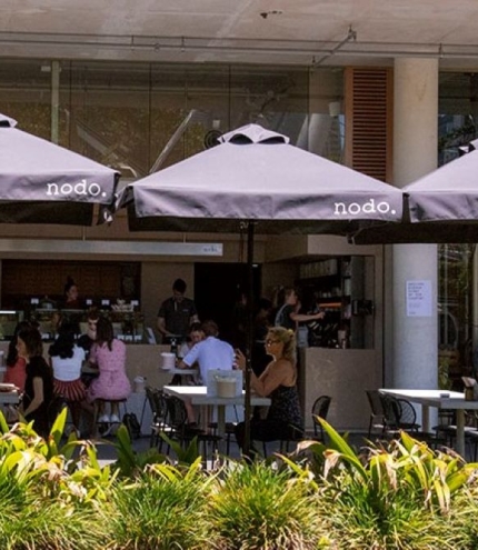 People sitting under umbrellas in courtyard at Nodo South 