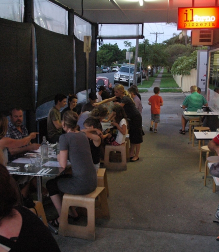 Diner seated on footpath eating pizza outside Il Forno Pizzeria in Sandgate