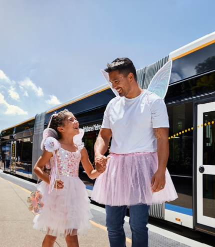 Dad and daughter in fairy costumes walking in front of the Brisbane Metro