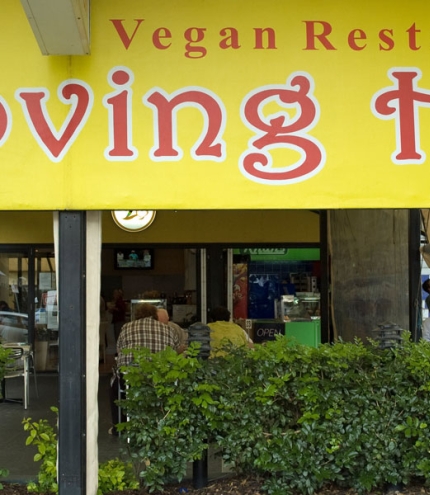 Loving Hut sign and hedge with diners sitting outside Loving Hut cafe Mt Gravatt