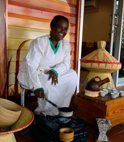 Female staff member in traditional dress roasting Ethiopian coffee beans over a little stove outside Mu'ooz African Eritrean Restaurant 