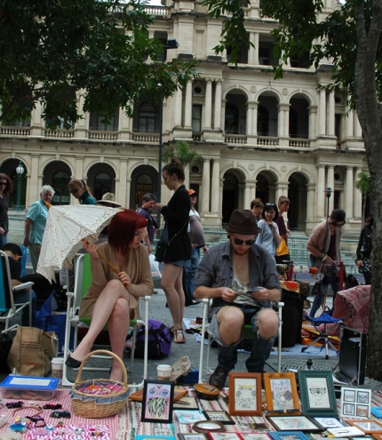 Market sellers with suitcases open full of clothes and objects next to Treasury Casino building.