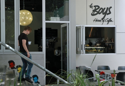 Waiter carrying cup of coffee walking down steps outside boys house of coffee in Kelvin Grove.