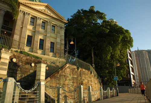 Jogger on footpath along Brisbane River with Customs House in the background at sunrise.