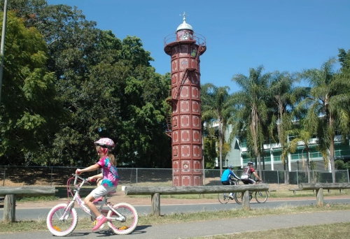 Kids riding a bike in front of Gas Stripping Tower near Davies Park in West End