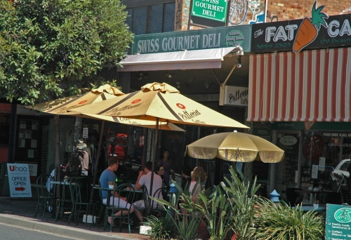 People sitting on Boundary Road under umbrellas outside Swiss Gourmet Deli