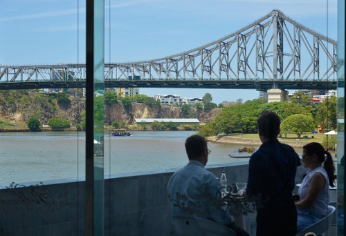 Couple sitting at table on deck overlooking the Story Bridge and Brisbane River