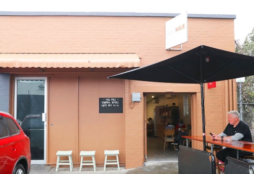 Man sitting under an umbrella at a table outside Mad Mile Coffee