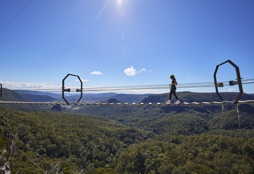 Woman on an 80-metre wobbly bridge at The Arête Via Ferrata Tour at Happitat Adventure Park 