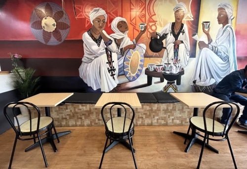 Tables and chairs in front of African mural at wall Afro Restaurant, Moorooka 