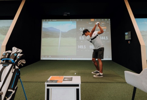 Man hitting a golf ball in a TrackMan Golf Simulator bay atThe Golf Bunker, Hamilton 