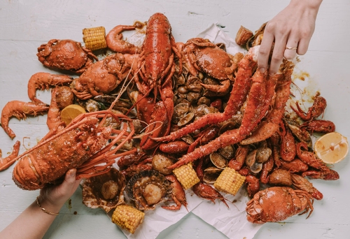 Two hands grabbing pieces of crab at Krabby’s Crab Boil, The Barracks, Petrie Terrace