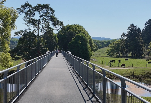 Cyclist on e-bike crossing rail bridge overlooking lush countryside