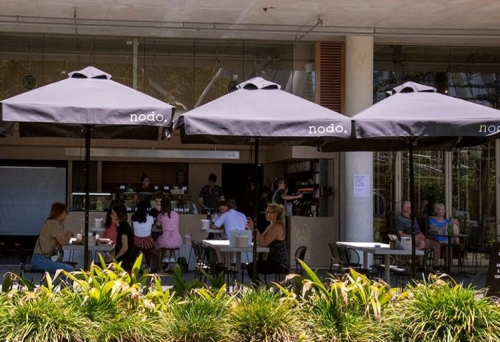 People sitting under umbrellas in courtyard at Nodo South 