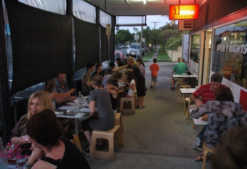 Diner seated on footpath eating pizza outside Il Forno Pizzeria in Sandgate