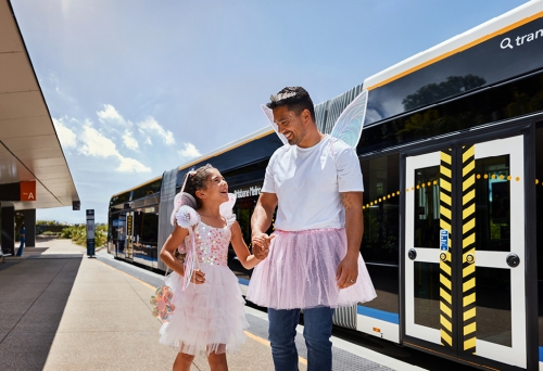Dad and daughter in fairy costumes walking in front of the Brisbane Metro